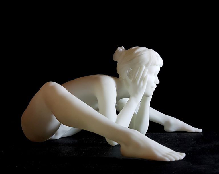 A white figurine of a nude woman siiting and leaning forward